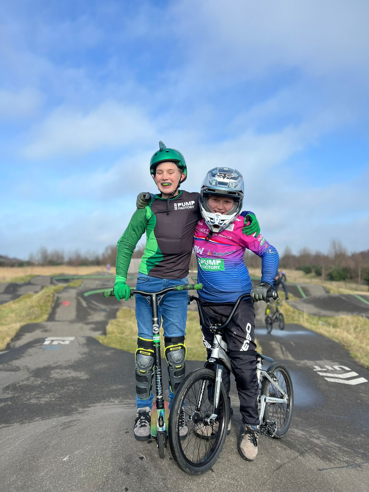 Twee vrienden op de pumptrack, één met scooter en één met BMX